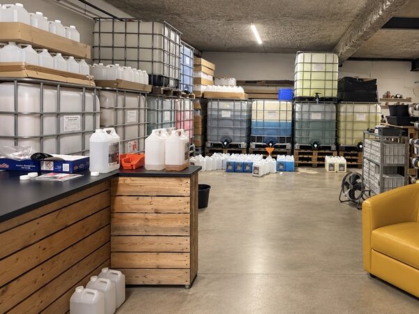 Cuves de 1000 litres alignées dans l’entrepôt, avec des bidons de 5 litres prêts au remplissage